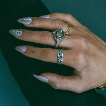 A hand model wearing a Sterling silver evil eye protection ring with faceted citrine in the eye's center, a silver leopard print stacking band, and a gold bone eternity ring.