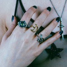 A sterling silver evil eye protection ring with peridot, a gold luna/crescent moon ring, and a silver twiggy branch ring on model's hands. A large silver dagger pendant necklace on model, Sterling silver evil eye protection ring with peridot, peridot ring, sterling silver ring, dripping eye ring, evil eye ring, hellhound jewelry ring, faceted peridot ring, gemstone ring, gemstone jewelry, gemstone